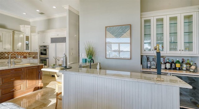 kitchen featuring light stone counters, sink, beverage cooler, crown molding, and double oven