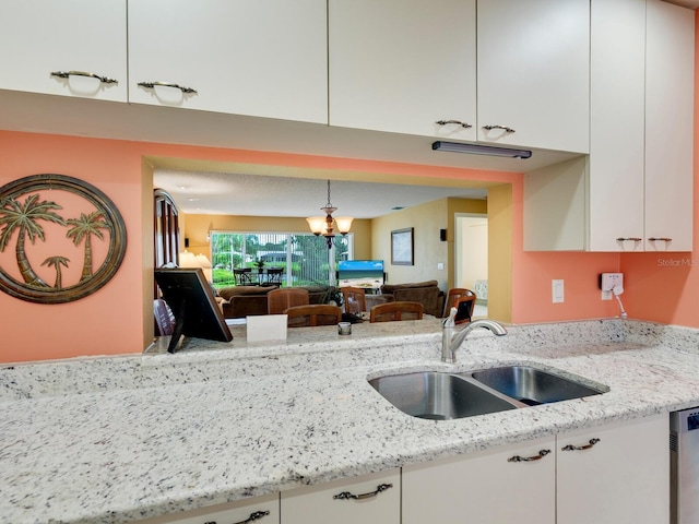 kitchen with white cabinetry, a notable chandelier, sink, and light stone counters