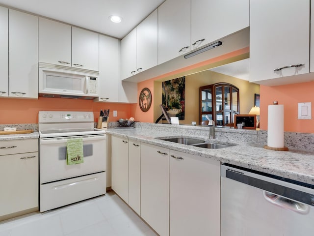 kitchen featuring white appliances, sink, light tile floors, light stone countertops, and white cabinetry