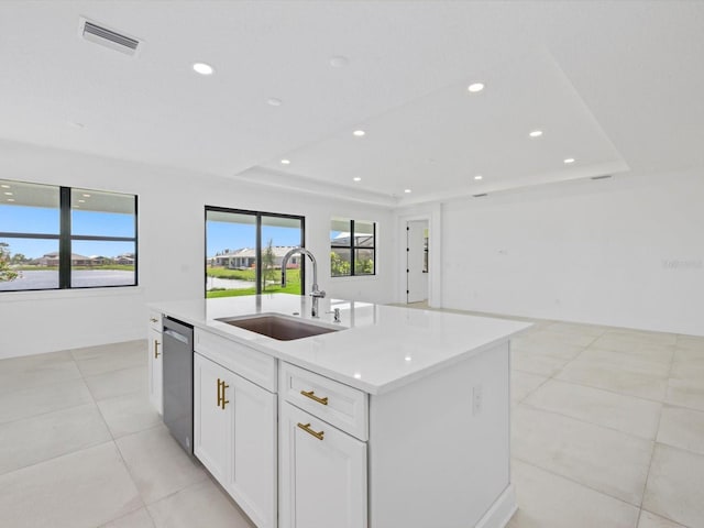 kitchen featuring a raised ceiling, sink, stainless steel dishwasher, a kitchen island with sink, and white cabinetry