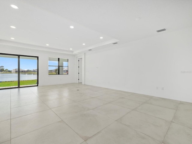 empty room featuring light tile patterned flooring, a water view, and a raised ceiling