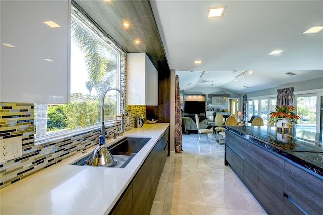 kitchen with sink, light tile floors, white cabinets, tasteful backsplash, and lofted ceiling