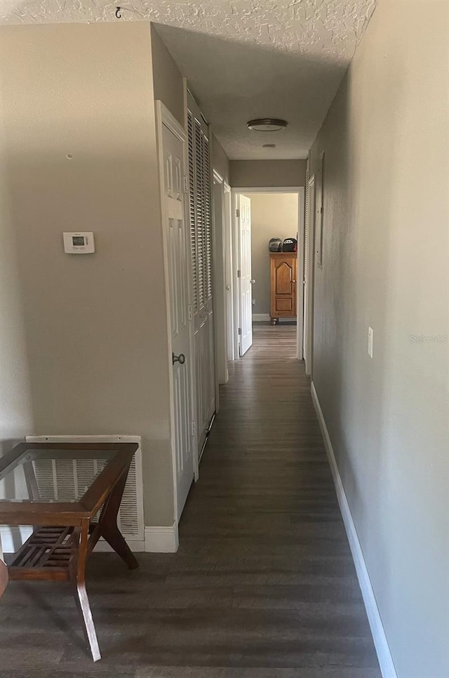 hallway with a textured ceiling and dark hardwood / wood-style flooring