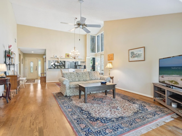 living room with a towering ceiling, ceiling fan with notable chandelier, and light wood-type flooring