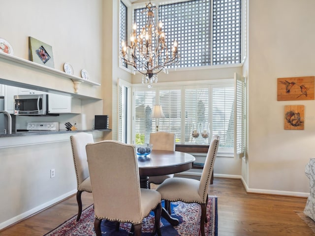 dining space with an inviting chandelier, dark wood-type flooring, and a towering ceiling