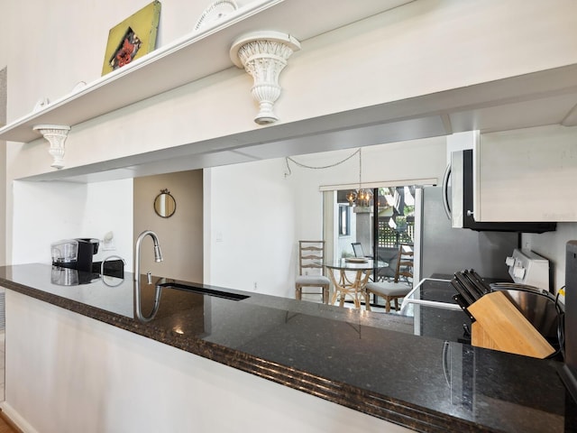 kitchen with decorative light fixtures, a notable chandelier, dark stone counters, range, and sink