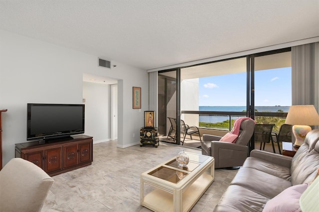 living room with a textured ceiling, expansive windows, light tile flooring, and a water view