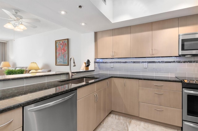 kitchen featuring ceiling fan, light tile flooring, appliances with stainless steel finishes, sink, and dark stone counters