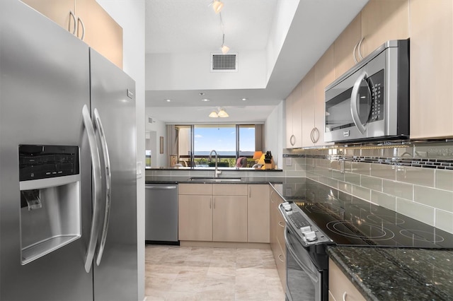 kitchen featuring stainless steel appliances, light tile floors, tasteful backsplash, dark stone countertops, and sink