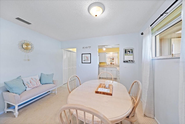 dining room with light carpet, ceiling fan, and a textured ceiling