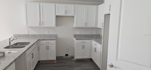 kitchen with white cabinetry, light stone counters, dark wood-style floors, and a sink