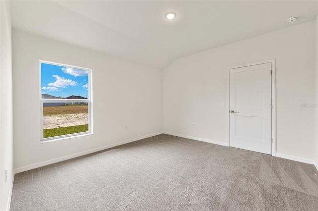 spare room featuring carpet flooring and vaulted ceiling