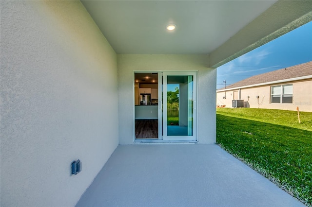 entrance to property featuring a patio area, a yard, and central AC