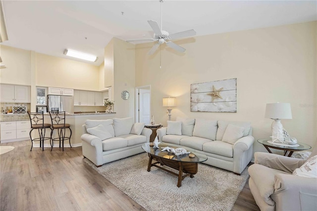 living room featuring ceiling fan, light hardwood / wood-style floors, and a towering ceiling