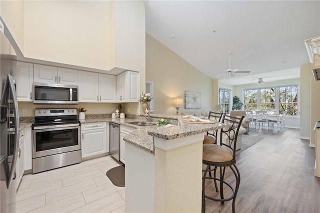 kitchen with kitchen peninsula, stainless steel appliances, sink, high vaulted ceiling, and a breakfast bar area