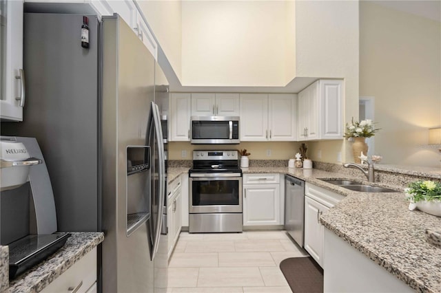 kitchen featuring appliances with stainless steel finishes, light stone counters, sink, light tile patterned floors, and white cabinets