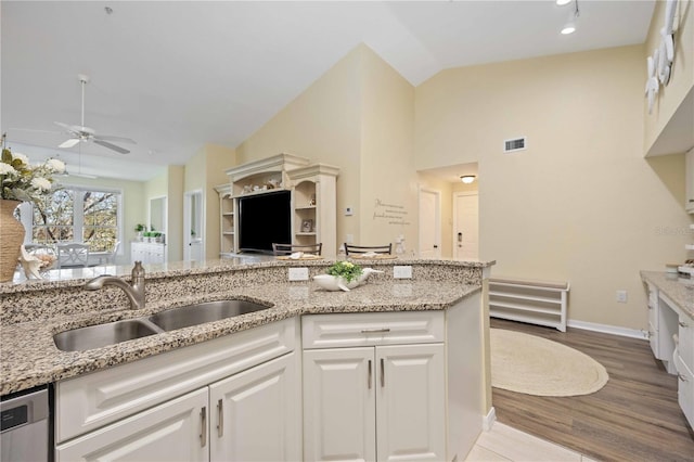 kitchen with white cabinets, sink, vaulted ceiling, light wood-type flooring, and light stone counters