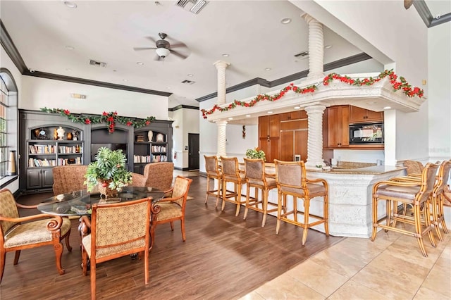 dining room featuring ceiling fan, light wood-type flooring, ornate columns, and ornamental molding