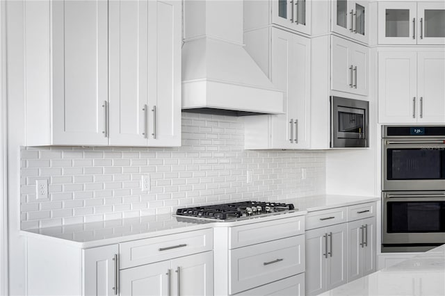 kitchen featuring custom exhaust hood, stainless steel appliances, backsplash, and white cabinetry