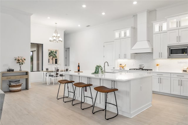 kitchen with custom range hood, white cabinetry, stainless steel appliances, a kitchen island with sink, and sink