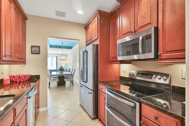 kitchen with an inviting chandelier, pendant lighting, dark stone counters, stainless steel appliances, and light tile floors