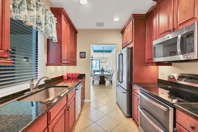 kitchen featuring appliances with stainless steel finishes, hanging light fixtures, dark stone countertops, light tile floors, and sink