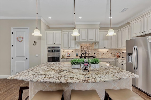 kitchen featuring a kitchen breakfast bar, appliances with stainless steel finishes, decorative light fixtures, and a kitchen island with sink