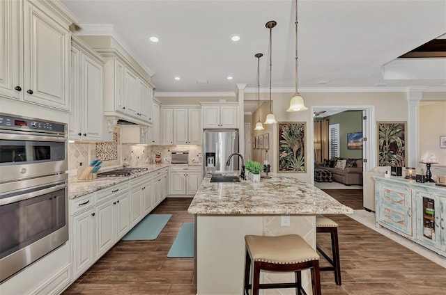 kitchen featuring dark hardwood / wood-style floors, a breakfast bar, a center island with sink, stainless steel appliances, and light stone countertops