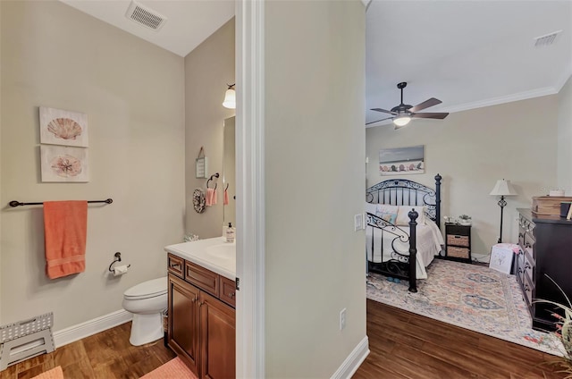 bathroom featuring toilet, ceiling fan, vanity, ornamental molding, and wood-type flooring