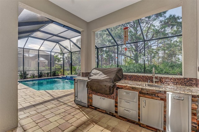 view of pool with area for grilling, a patio area, sink, glass enclosure, and exterior kitchen