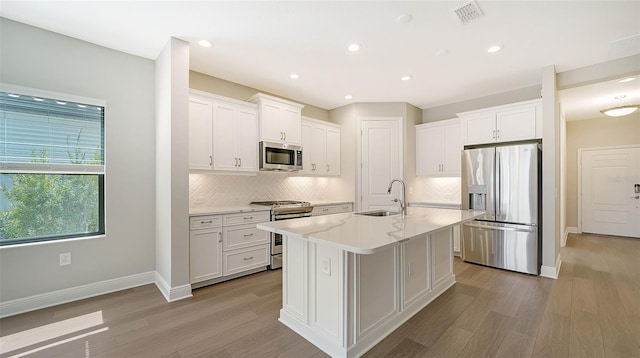 kitchen featuring white cabinets, stainless steel appliances, a kitchen island with sink, and sink