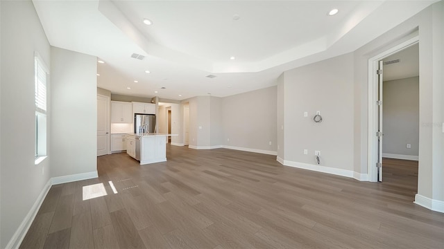 unfurnished living room with a tray ceiling and light wood-type flooring