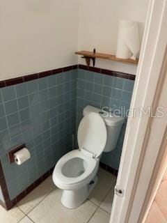 711A Pineland Ave, Venice, FL 34285 - bathroom featuring toilet, tile patterned flooring, a wainscoted wall, and tile walls
