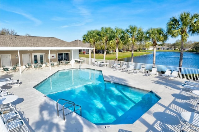 community pool with a patio area, fence, and a water view