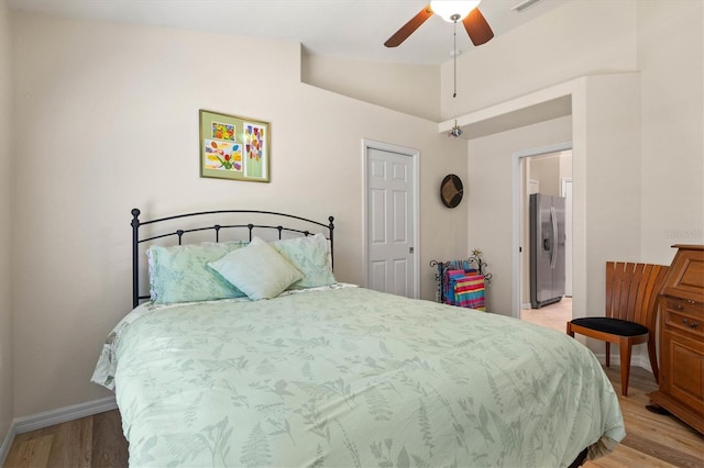 bedroom with stainless steel refrigerator with ice dispenser, light wood finished floors, vaulted ceiling, ceiling fan, and baseboards