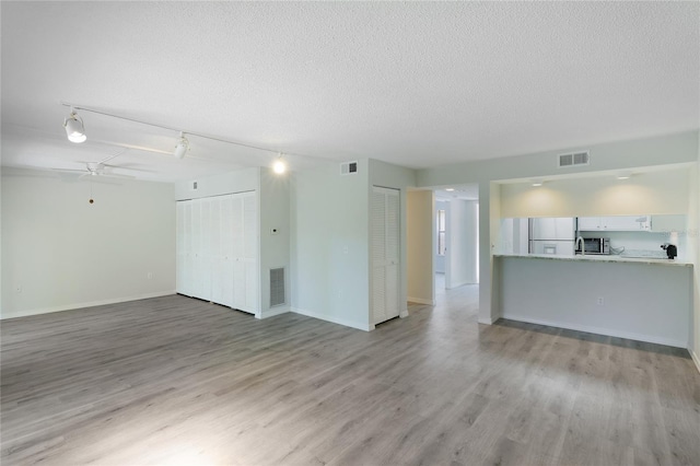 unfurnished living room featuring a textured ceiling, light wood-type flooring, track lighting, and ceiling fan