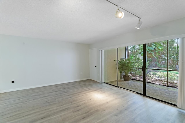 spare room with light hardwood / wood-style flooring, track lighting, and a textured ceiling