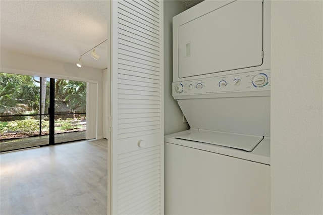 washroom featuring a textured ceiling, light hardwood / wood-style floors, and stacked washer and clothes dryer