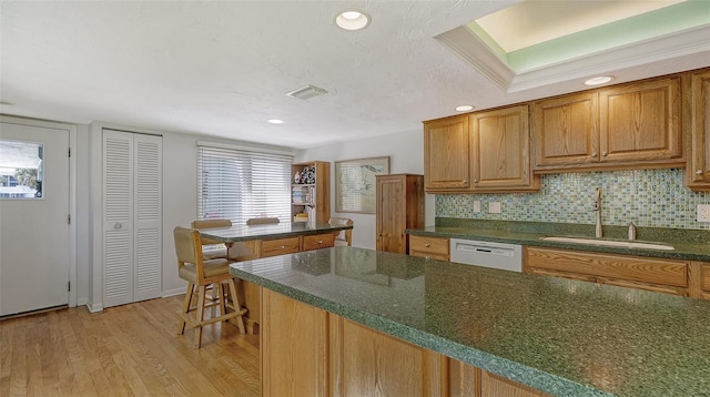 kitchen featuring tasteful backsplash, sink, a kitchen bar, white dishwasher, and light hardwood / wood-style flooring