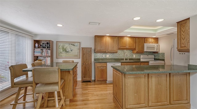 kitchen featuring sink, a tray ceiling, white appliances, light hardwood / wood-style floors, and decorative backsplash