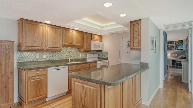 kitchen featuring white appliances, a raised ceiling, sink, and light hardwood / wood-style flooring