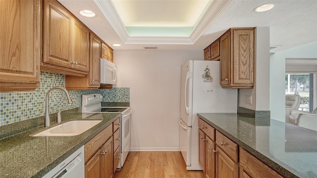 kitchen featuring sink, backsplash, light hardwood / wood-style floors, a raised ceiling, and white appliances