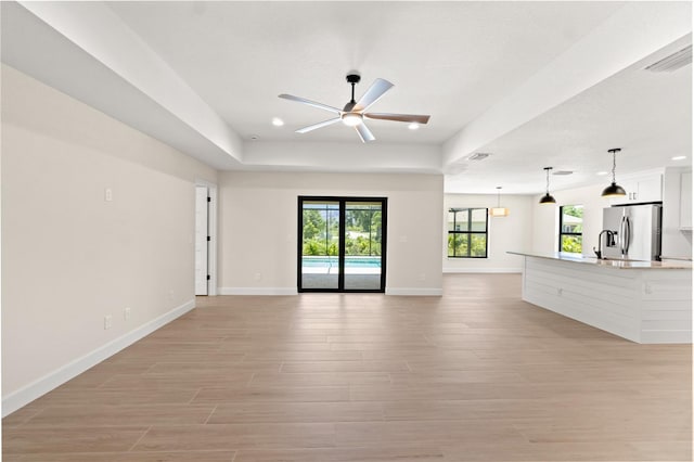 unfurnished living room featuring baseboards, visible vents, a ceiling fan, light wood-style floors, and a tray ceiling