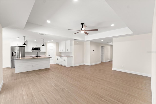 unfurnished living room featuring a tray ceiling, light wood-style flooring, recessed lighting, baseboards, and a ceiling fan