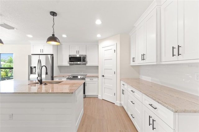 kitchen with appliances with stainless steel finishes, light stone countertops, white cabinetry, and hanging light fixtures