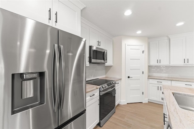 kitchen with appliances with stainless steel finishes, white cabinets, tasteful backsplash, and light hardwood / wood-style flooring