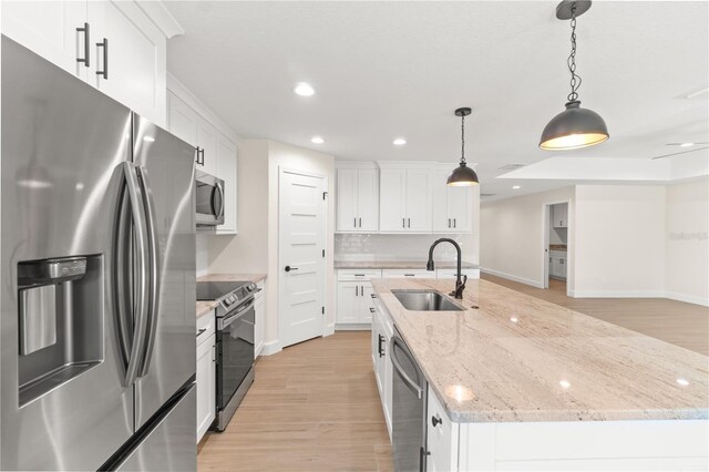 kitchen featuring white cabinets, stainless steel appliances, backsplash, a center island with sink, and sink