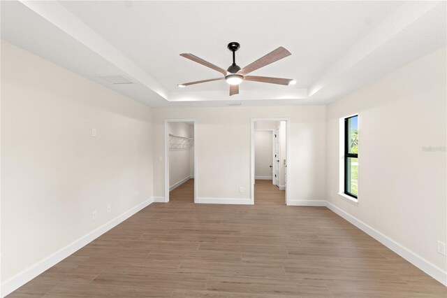 unfurnished bedroom with a walk in closet, light wood-type flooring, a closet, ceiling fan, and a raised ceiling