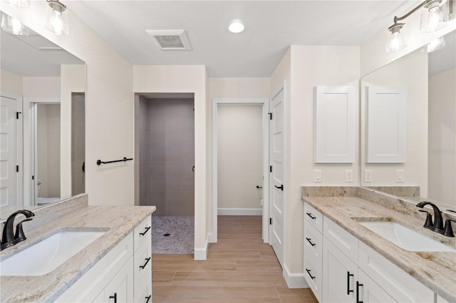 bathroom with wood finish floors, walk in shower, a sink, and visible vents