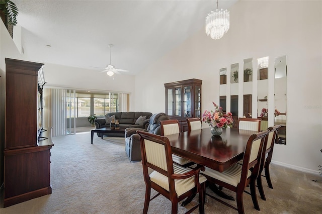 carpeted dining space with ceiling fan with notable chandelier and high vaulted ceiling